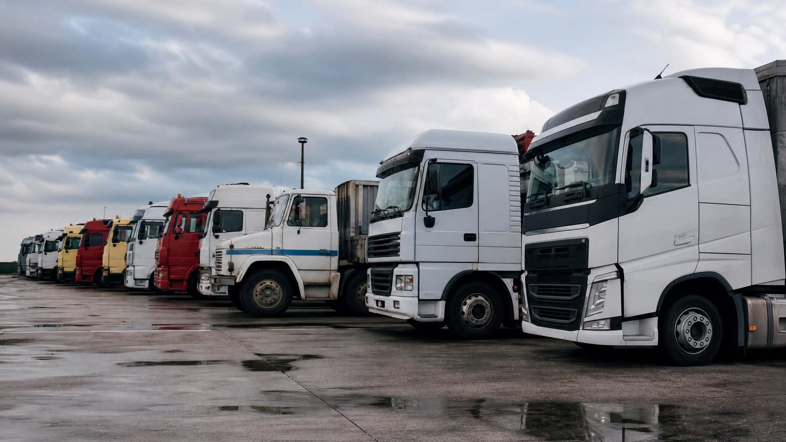 Caminhões de diferentes idades enfileirados em pátio de transportadora